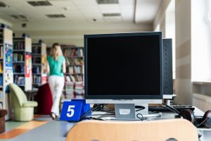 public computers at the library, a lady walking away toward books in the background